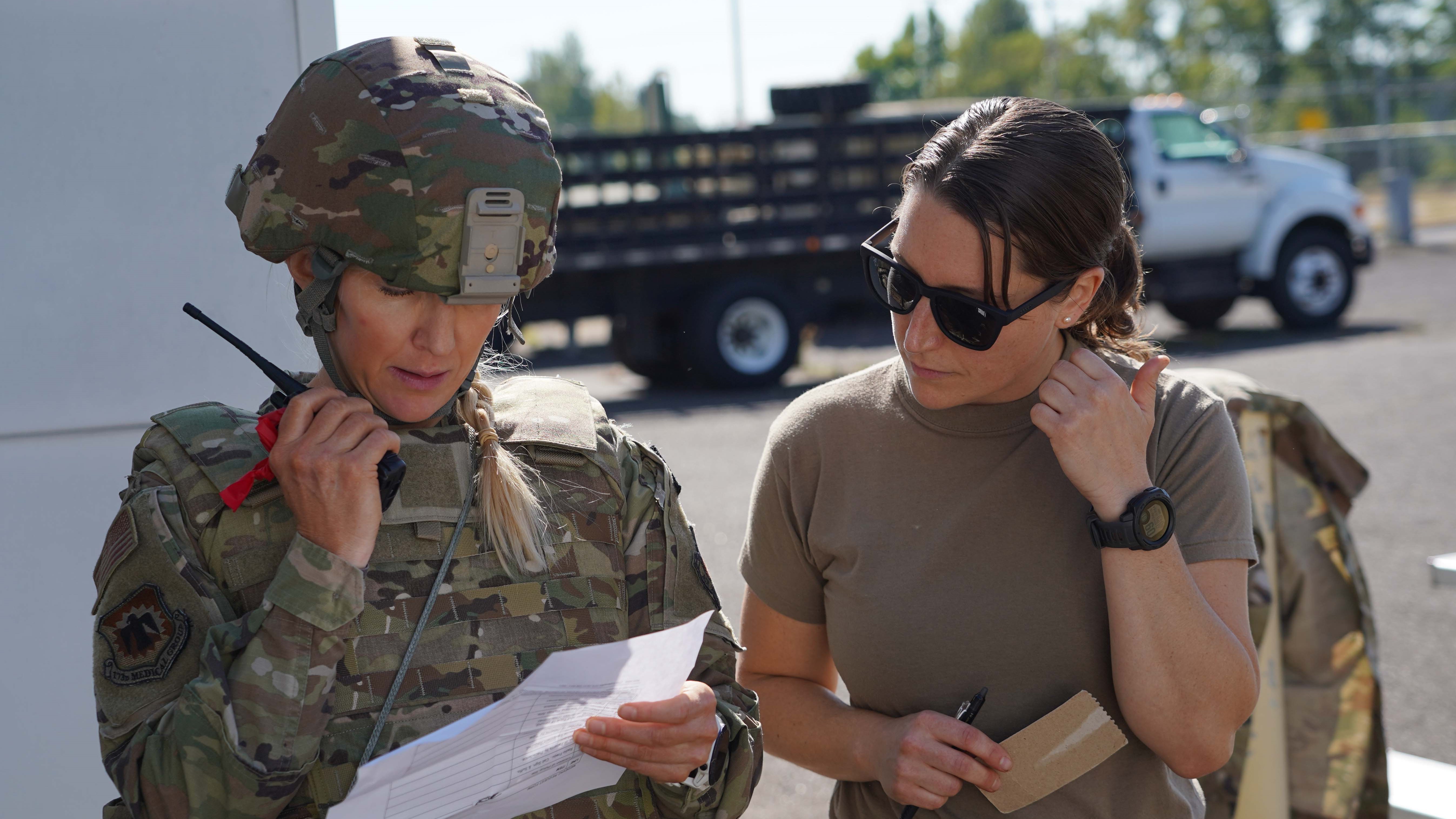 Two service members looking at a piece of paper and talking into a walkie-talkie