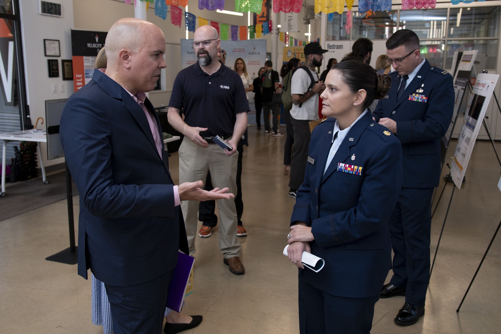 Military and civilian personnel in an exhibit hall, talking