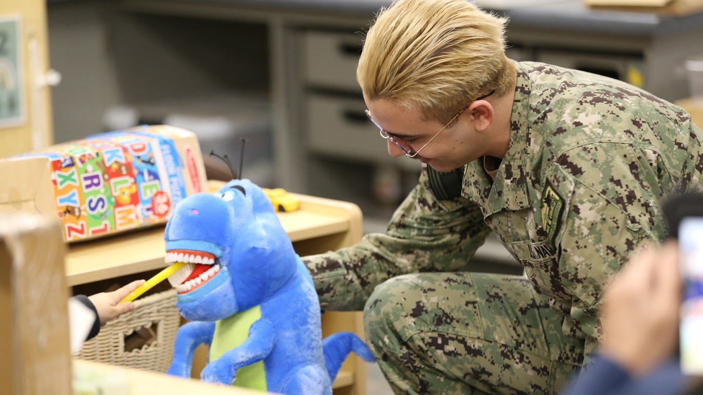 Hospital Corpsman 3rd Class Julian Salinas from Naval Health Clinic Lemoore's dental clinic helped students at Admiral Akers School practice proper teeth brushing on a stuffed dinosaur. (U.S. Navy photo by Elaine Heirigs Naval Health Clinic Lemoore/Navy Medicine Readiness and Training Command Lemoore Public Affairs)