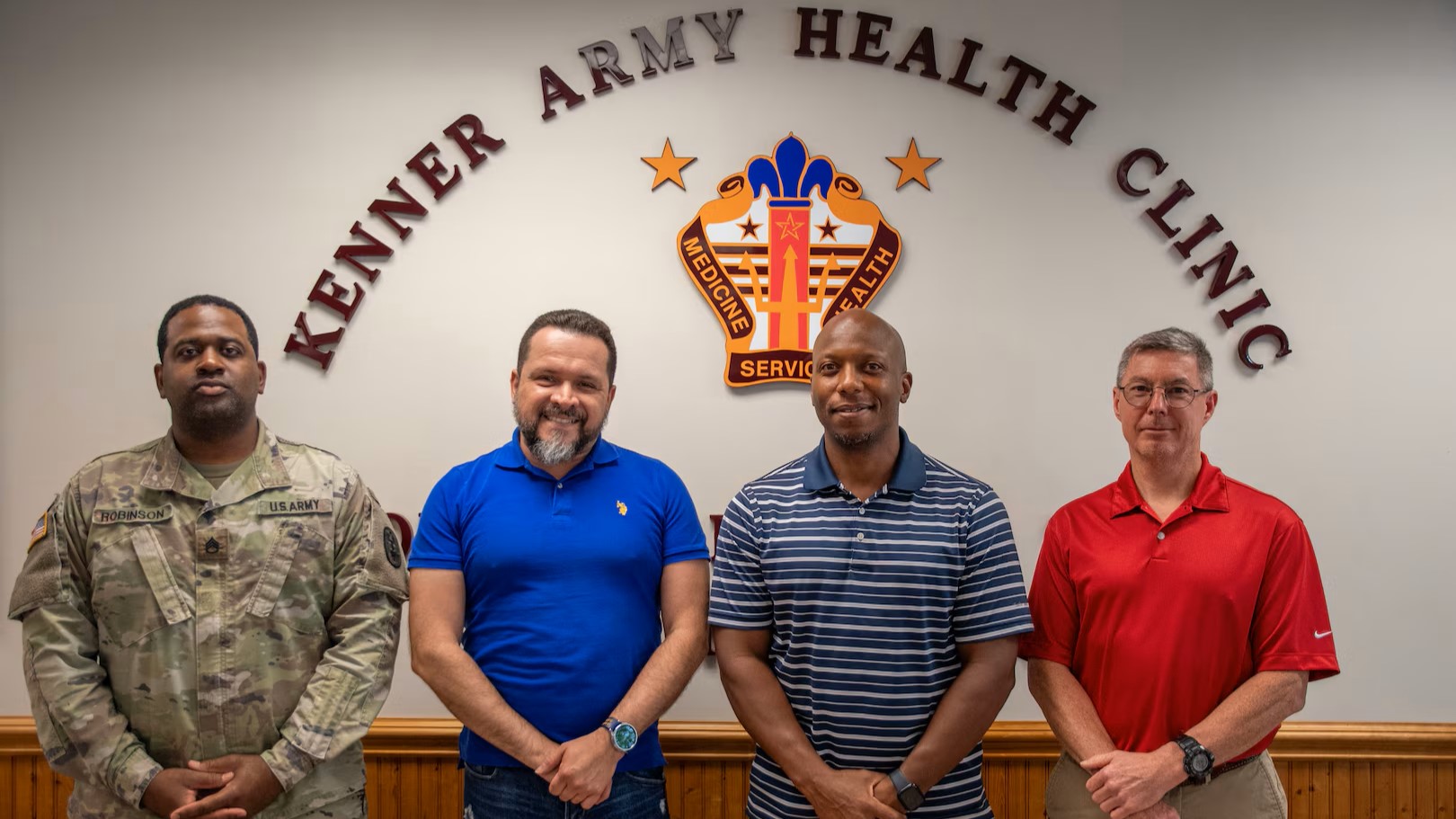 Four service members standing in front of a sign that says "Kenner Army Health Clinic."
