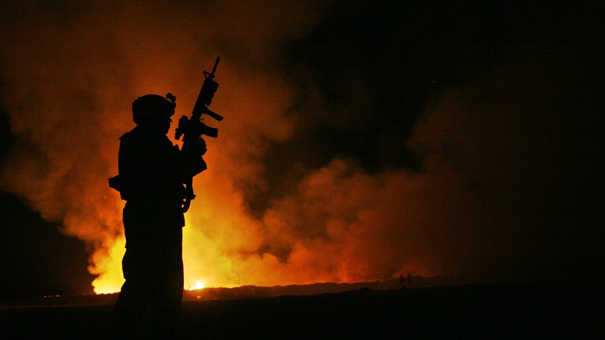 Sgt. Robert B. Brown from Fayetteville, N.C. with Regimental Combat Team 6, Combat Camera Unit watches over the civilian Fire Fighters at the burn pit as smoke and flames rise into the night sky behind him