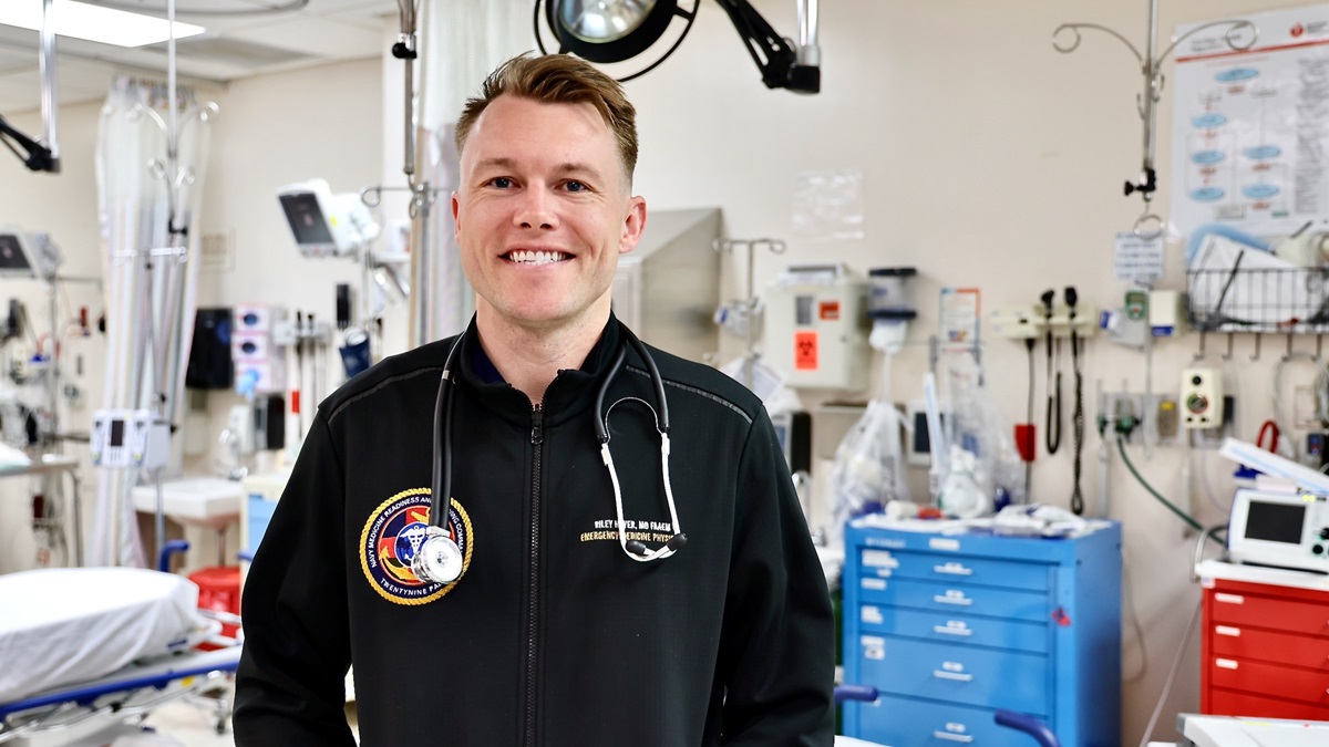 Lt. Cmdr. Riley Hoyer, an emergency physician and Department Head of Emergency Medicine at Naval Hospital Twentynine Palms, stands inside the hospital’s emergency department a week after his swift response to a life-threatening emergency in downtown Palm Springs on March 20, 2025. While on an evening jog, Hoyer encountered a teenage boy suffering from a severe stab wound behind his knee, resulting in significant blood loss. Acting quickly, he stabilized the victim by adjusting a makeshift tourniquet before collaborating with local law enforcement to apply a proper tourniquet, successfully controlling the hemorrhage. His immediate intervention, tactical medical training, and composure under pressure helped save the teen’s life before emergency medical services arrived. Hoyer credits his Navy training in Tactical Combat Casualty Care (TCCC) for equipping him with the skills necessary to provide rapid, lifesaving aid in unpredictable situations (U.S. Navy photo by Christopher C. Jones, NHTP/NMRTC Twentynine Palms public affairs officer).