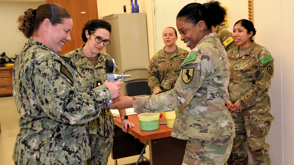 A Medical Education and Training Campus Occupational Therapy Assistant student guides OTA instructor, Hospital Corpsman 1st Class Lindsey Pruett, on using a dynamometer to assess hand grip strength as Lt. Cmdr. Cynthia DeArmon, OTA course director, and fellow students observe.