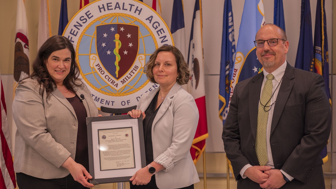 Kathleen L. Berst, left, presents an official charter to Kendra Lawrence, Ph.D., during an Operational Medical Systems Program Management Office chartering ceremony, Fort Detrick, Md., April 10, 2025. Berst is the Acting Assistant Director Support/Component Acquisition Executive for the Defense Health Agency and Lawrence is the project manager for OPMED PMO’s Warfighter Protection and Acute Care Project Management Office