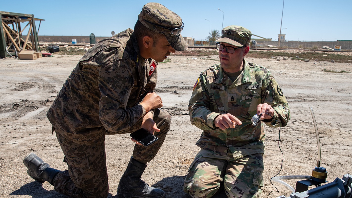 U.S. Army Staff Sgt. Mark Faria, a preventive medicine specialist assigned to the 903rd Medical Detachment Preventive Medicine, a U.S. Army Reserve unit based in Machesney Park, Illinois, shows a Tunisian Armed Forces service member the deployable particulate sampler system to collect air samples which analyzes particulates for contaminants and concentration during African Lion 2025 (AL25) at the Port of Gabes, Tunisia, April 18, 2025.