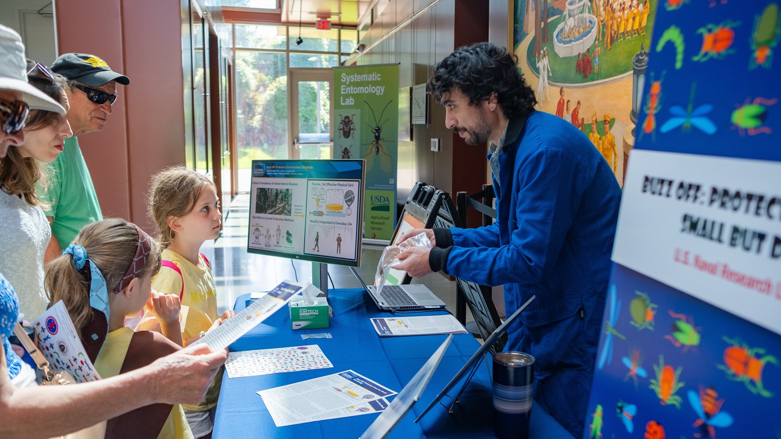 Dr. Javier Jimenez (right), research chemist at the U.S. Naval Research Laboratory, presents an insect repellent gel to visitors at Bugapalooza, an annual event held at the National Museum of Health and Medicine in Silver Spring, Maryland, June 21, 2025.