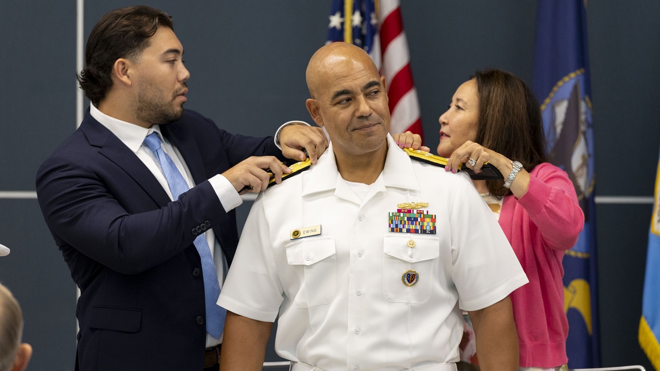 Rear Adm. Reginald “Reg” S. Ewing III, director of the Defense Health Network National Capital Region (DHN, NCR), looks on as he receives his new shoulder boards from his wife, Mina, and son Kendall, during a promotion ceremony at the USO on Naval Support Activity Bethesda, Friday, July 18.