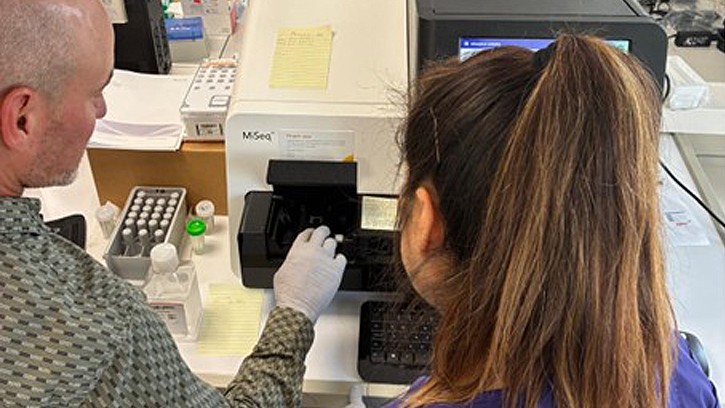 William Gruner, a molecular biologist with the U.S. Air Force School of Aerospace Medicine 711 Human Performance Wing, and Pilar Mandujano, a laboratory technician with Landstuhl Regional Medical Center, prepare the Illumina MiSeq for genomic characterization of influenza virus samples. (Defense Health Agency Public Health photo by Lindsay Morton, Armed Forces Health Surveillance Division Global Emerging Infections Surveillance Branch)