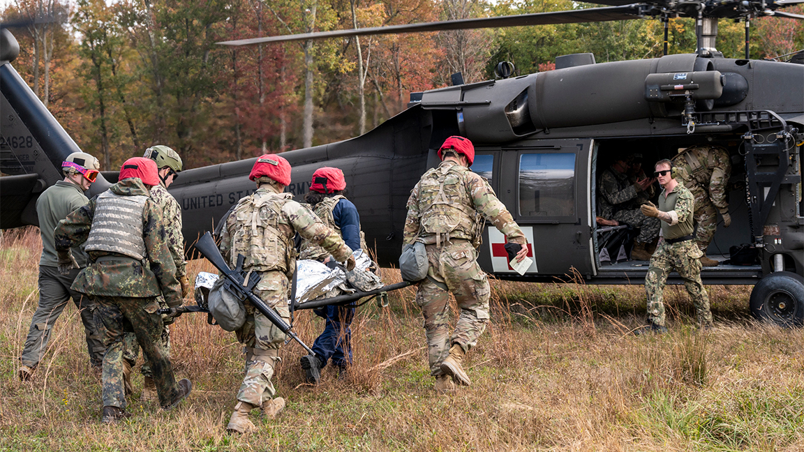 Navy Hospital Corpsman 1st Class Jonathan Shumaker, USU and DoD’s Service Member of the Year, signals to an incoming medical team carrying a patient to a medevac helicopter during the University’s annual Bushmaster exercise. (Photo credit: Tom Balfour, USU)
